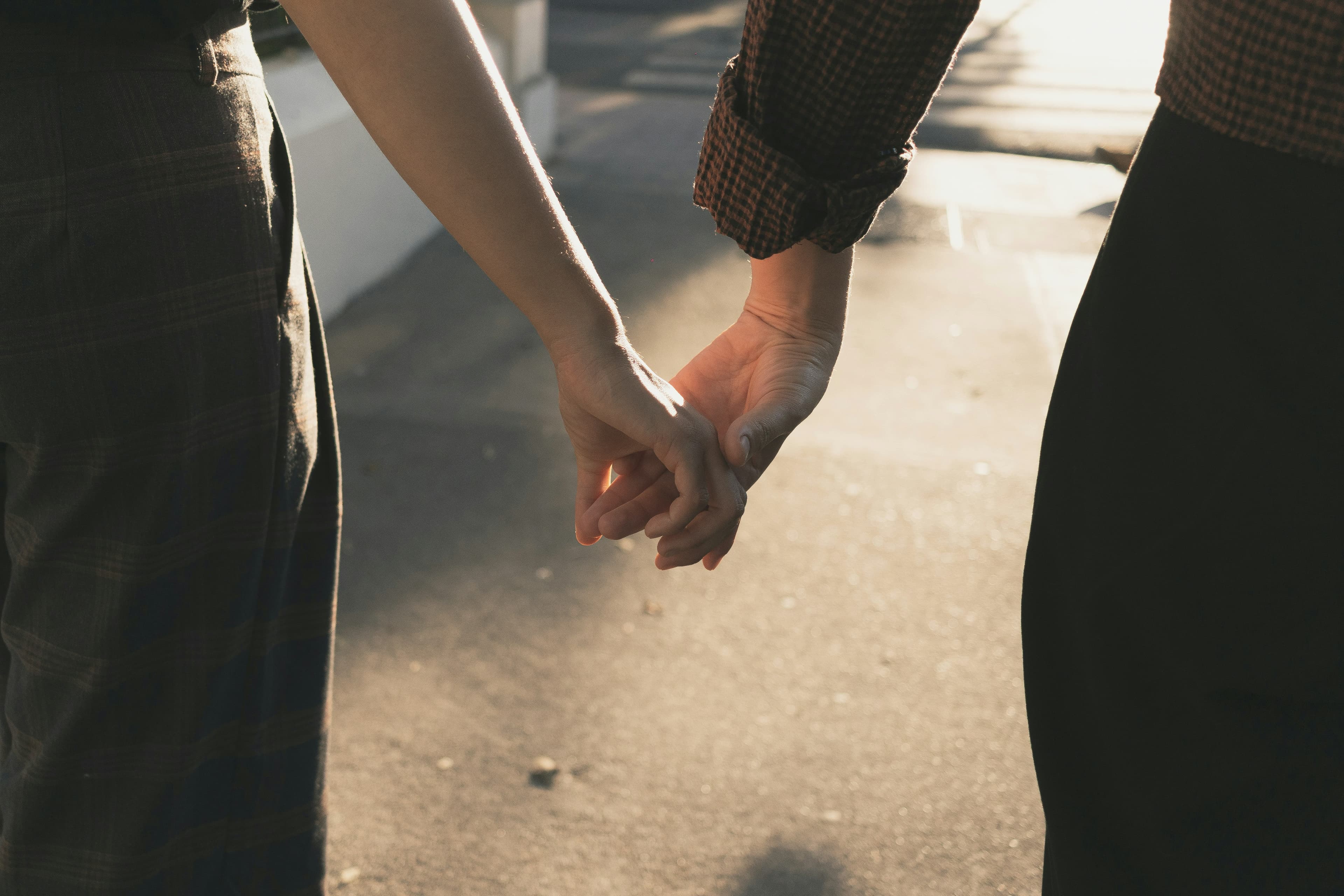 Two people holding hands while walking on a sunlit sidewalk, with soft shadows cast on the ground.