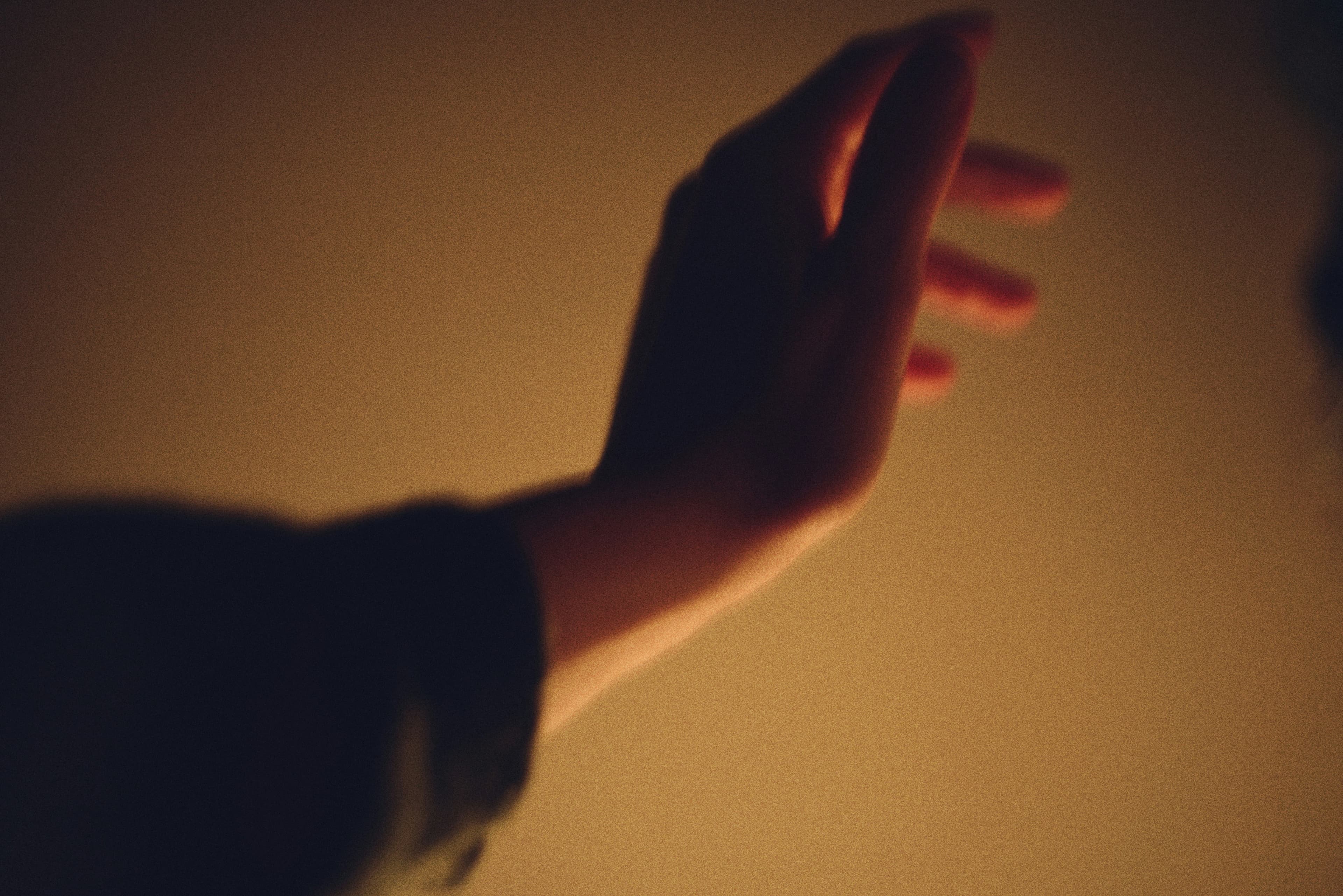 A hand reaching upwards against a warm, softly lit background, creating a sense of movement and warmth.